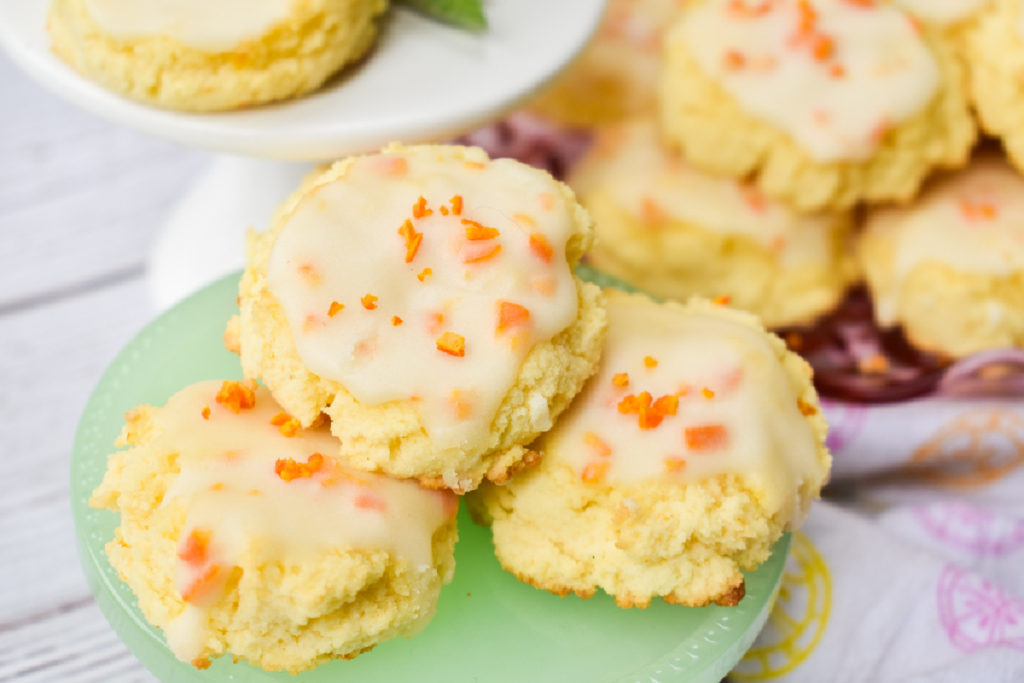 keto orange cookies on green pedestal with more cookies on pink plate in background