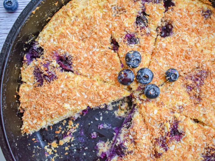 keto blueberry toasted coconut skillet cake in cast iron skillet with one slice missing close up