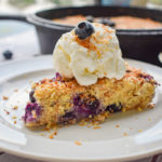 keto blueberry toasted coconut skillet cake slice topped with ice cream with cast iron and blueberries in the background