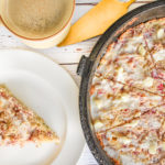 keto raspberry white chocolate scones in cast iron skillet cut into slices with one slice removed and slice on white plate on the left and cup of coffee