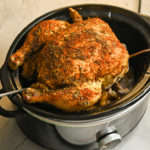 keto whole chicken lifted out of a crockpot with two metal spatulas